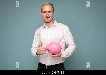 Portrait de heureux positif souriant jeune beau blond homme d'affaires avec des émotions sincères portant décontracté blanc chemise isolée sur bleu Banque D'Images