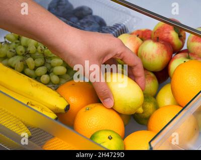 Une femme reçoit un citron du tiroir du réfrigérateur rempli de fruits.Gros plan. Banque D'Images