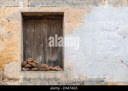 Concept de maison abandonnée.Fenêtre vieillie avec des volets en bois maintenus fermés avec pile de pierres sur le seuil pelé fendu vide blanc dans une partie de wal Banque D'Images