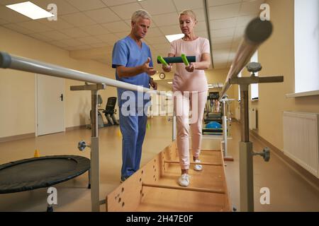 Physiothérapeute aidant les patients matures à marcher entre les barres parallèles à l'hôpital Banque D'Images