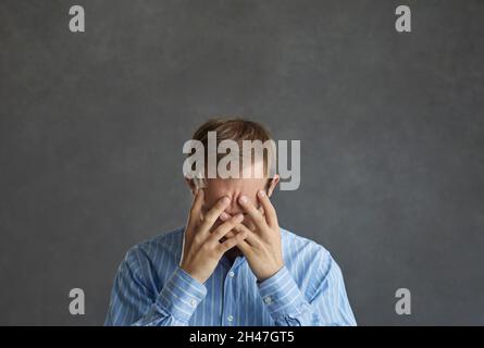 Frustré et désespéré, il cachait le visage dans ses mains sur fond de studio gris Banque D'Images