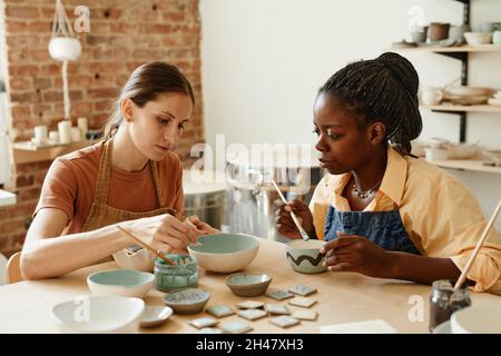 Portrait aux tons chauds de deux jeunes femmes profitant d'un atelier de poterie dans un studio confortable, espace de copie Banque D'Images