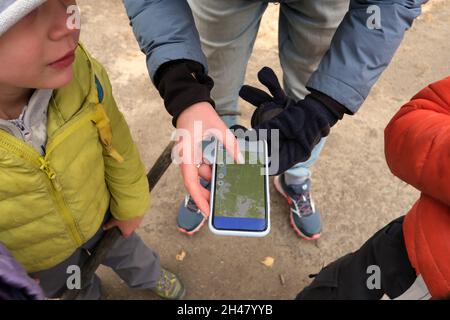 Du dessus de la récolte femelle méconnaissable montrant une carte sur écran de téléphone portable moderne aux enfants sans visage pendant le camping dans la nature Banque D'Images