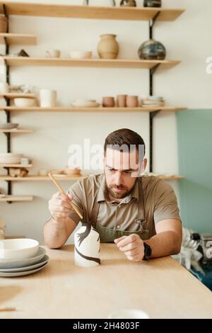Portrait ton chaud de l'homme barbu créateur décorant la céramique dans l'atelier de poterie, l'espace de copie Banque D'Images