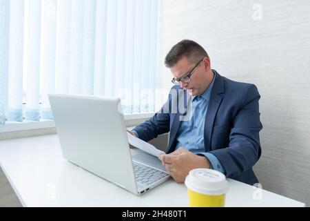 Un jeune homme d'affaires désespéré dans son bureau à la recherche de documents papier. un employé de bureau étudie intensément les contrats Banque D'Images