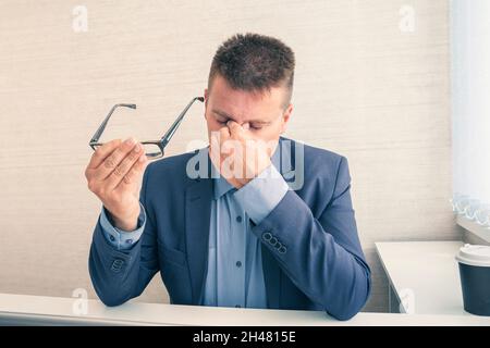Travailler à domicile, fatigués ou fatigués.Un jeune homme d'affaires asiatique est assis sur un bureau. Fatigué, stressé, il tient le nez. Fermez les yeux après Banque D'Images