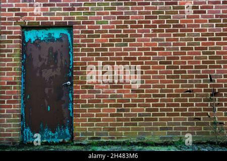 Qu'est-ce qui se cache derrière la porte verte ? : détail extérieur d'Un mur de briques et d'une porte verte défraîchi à la dangereuse usine de lait torridge Vale, Torrington Banque D'Images