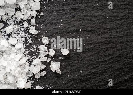 Gros plan de cristaux de sel de mer sur ardoise de pierre.Capture macro de sel sur surface noire, vue de dessus, espace pour le texte Banque D'Images