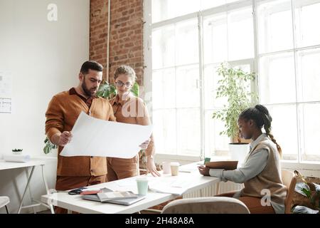 Portrait d'un homme barbu tenant des plans de projet tout en travaillant avec l'équipe de conception créative en studio, espace de copie Banque D'Images