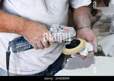 Par-dessus la récolte, un maître masculin méconnaissable utilisant un polisseur électrique tout en créant un nouveau souvenir en marbre dans un atelier traditionnel Banque D'Images