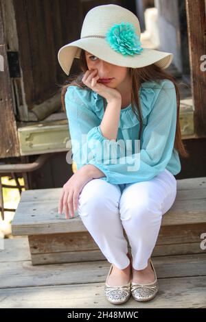 Une jeune fille solitaire pensive de 11 ans en haut bleu et chapeau de paille Banque D'Images