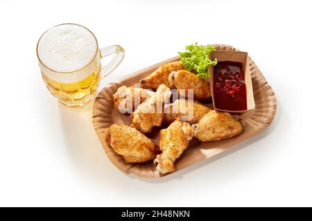 Ailes de poulet et ketchup servis sur fond blanc avec un verre de bière lager Banque D'Images