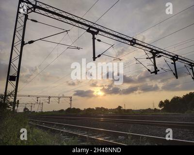 Lignes aériennes au-dessus des voies ferrées vides contre un ciel bleu nuageux au coucher du soleil Banque D'Images