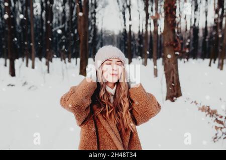 Photo de jeune belle femme en fourrure debout sur la neige blanche en forêt d'hiver.La fille est souriante et heureuse avec les yeux fermés.La femme a l'hiver Banque D'Images