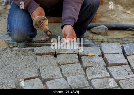 Gros plan sur l'installation et la pose de pierres sur le trottoir de la route par un travailleur de la construction Banque D'Images