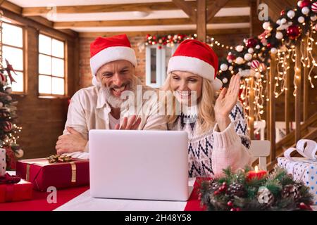 Joyeux couple mûr saluant la famille lors de l'appel vidéo de Noël avec des cadeaux. Banque D'Images