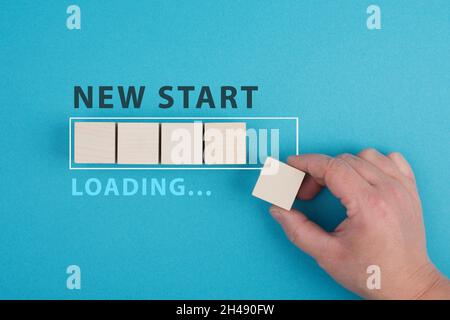 Mots nouveau départ avec une barre de chargement, main met le dernier cube en bois sur le fond bleu, message Banque D'Images