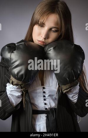 portrait créatif d'une femme d'affaires triste et fatiguée en gants de boxe.Arrière-plan gris Banque D'Images