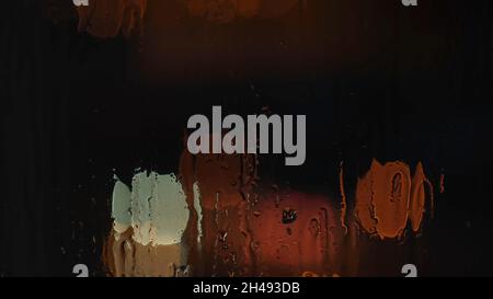 Humidifiez la fenêtre avec le fond de la ville nocturne avec de faibles lumières bokeh.Gros plan sur les gouttes d'eau de pluie qui s'en trouvent sur le flou coloré Banque D'Images