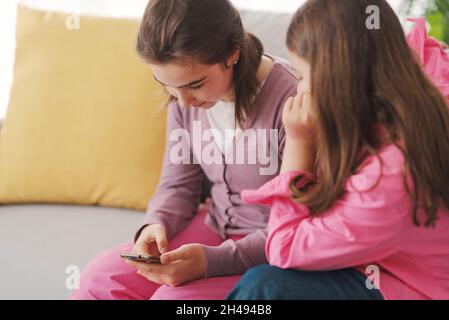 De jolies jeunes filles assises sur le canapé dans le salon et utilisant un smartphone ensemble Banque D'Images