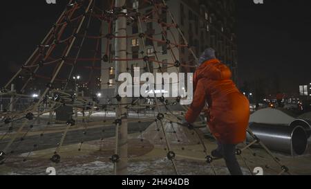 Fille qui court sur le terrain de jeu en hiver.Action.Une fille court dans le terrain de jeu en hiver.Vue arrière d'une fille qui court et joue dans l'aire de jeux. Banque D'Images