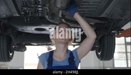 Femme mécanicien travaillant sous une voiture dans l'atelier de réparation automobile, elle vérifie l'absence de fuites Banque D'Images