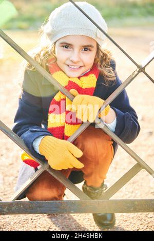 jeune fille souriante en manteau bleu derrière des barres de métal dans le parc en automne.Photo de haute qualité Banque D'Images