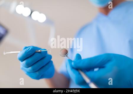 Dentiste mâle caucasien portant un masque facial tenant des outils dentaires à la clinique dentaire moderne Banque D'Images