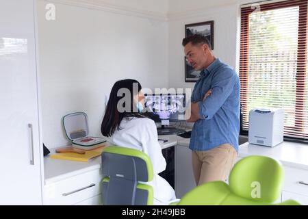 Dentiste biracial femelle portant un masque facial examinant les dents d'un patient mâle à la clinique dentaire moderne Banque D'Images