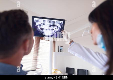 Dentiste biracial femelle portant un masque facial examinant les dents d'un patient mâle à la clinique dentaire moderne Banque D'Images