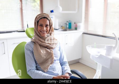Portrait d'une patiente biraciale souriante assise à une clinique dentaire moderne Banque D'Images