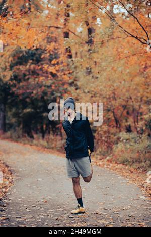 Jeune homme noir de course mixte s'étire quatre fois ou avant une course dans les bois sur un sentier pavé à l'automne.Port d'un casque d'activité.Homme en bonne santé courant Banque D'Images