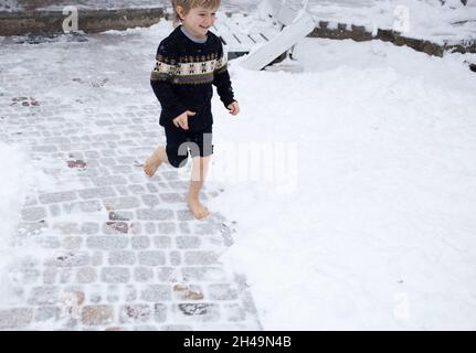 le garçon pieds nus de 4-5 ans court joyeusement dans la neige. concept de soins de santé, durcissement, chute de neige, temps froid. vacances actives d'hiver.Aime le Mo Banque D'Images