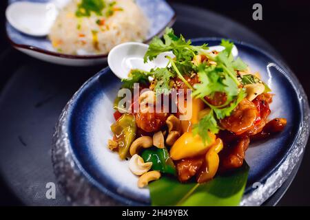 Un plat avec sauce barbecue et noix de cajou sur une assiette ronde bleue, garni d'herbes. Banque D'Images