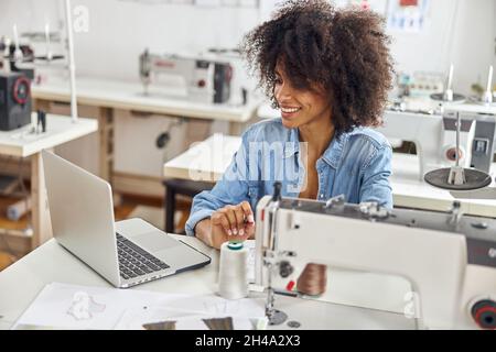 Une jeune femme afro-américaine positive sur mesure regarde la leçon vidéo via un ordinateur portable moderne assis sur le lieu de travail Banque D'Images
