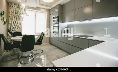 Cuisine moderne entièrement équipée avec appareils de cuisine en gris vert et blanc. Table et chaise. Journée ensoleillée Banque D'Images