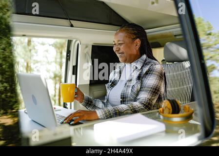 Femme noire parcourant un ordinateur portable et buvant une boisson Banque D'Images