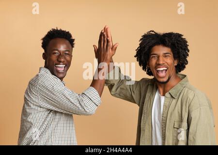 Deux gars noirs joyeux donnant le High Five les uns aux autres, amis afro-américains positifs du millénaire célébrant quelque chose, en riant et en s'amusant à Banque D'Images