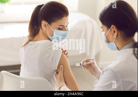 Jeune femme dans le masque médical de visage recevoir la grippe ou l'injection de vaccin Covid dans son bras Banque D'Images