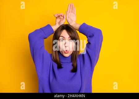 Photo de drôle douce jeune dame vêtue violet chandail montrant les bras de lapin mains tête isolé couleur jaune fond Banque D'Images