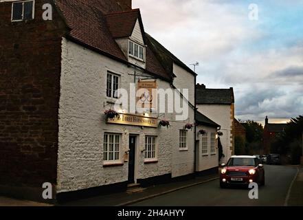 Le pub Three Horseshoes, une maison libre, dans le village rural d'Ecton dans le Northamptonshire comme une mini voiture passe au crépuscule. Banque D'Images