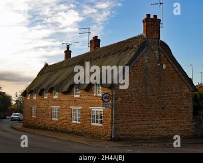 Cottages à toit de chaume sur High Street à Ecton, les pierres de la construction en pierre de l'iron du Northamptonshire sont réchauffées par le soleil du matin. Banque D'Images