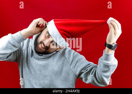 Un homme joyeux barbu dans un chapeau de Père Noël rouge tire le bubo de ce chapeau sur le côté. Banque D'Images
