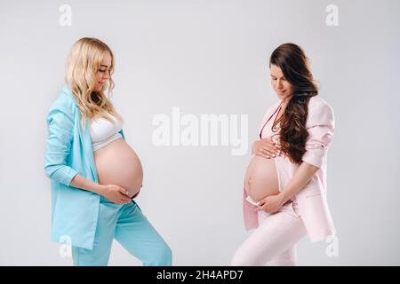 Deux femmes enceintes avec de gros ventre en costume sur fond gris. Banque D'Images