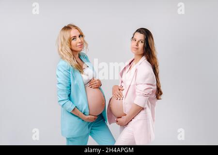 Deux femmes enceintes avec de gros ventre en costume sur fond gris. Banque D'Images