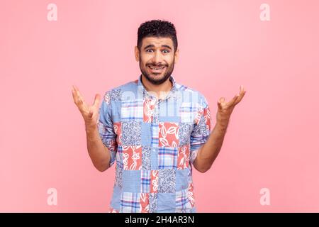 Portrait d'un jeune homme adulte confus ou choqué avec une barbe dans une chemise bleue décontractée debout avec les bras relevés et regardant la caméra demander.Studio d'intérieur isolé sur fond rose. Banque D'Images