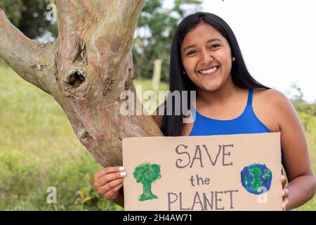 Une jeune fille adulte tient une affiche appelant à sauver la planète tout en embrassant un arbre.Portrait de la femme brune sur un fond naturel.ENREGISTREZ LE Banque D'Images