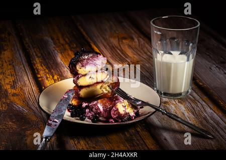 tranches de cheesecakes avec confiture de myrtille et crème sure sur une assiette avec un verre de lait sur la table. Banque D'Images