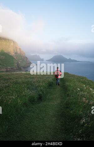 Randonnée dans le village de Gasadalur, îles Féroé.Un touriste avec un sac à dos marche le long du sentier sur l'île de Vagar Banque D'Images