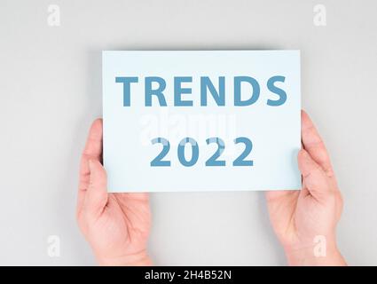 Tendances 2022 est debout sur un papier, mains tenant le signe, communication, marketing, nouveaux concepts, fond gris Banque D'Images